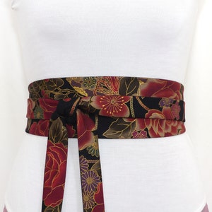 May include: A black fabric belt with a floral pattern in shades of red, gold, and purple. The belt is tied in a bow at the front.