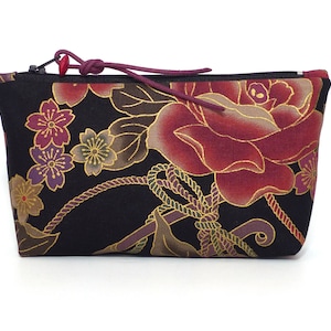 May include: A black zippered pouch with a floral print featuring red roses, gold accents, and purple and gold cherry blossoms.