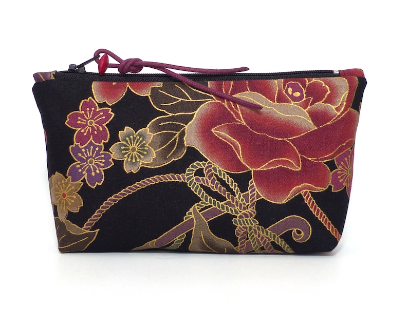 May include: A black zippered pouch with a floral print featuring red roses, gold accents, and purple and gold cherry blossoms.