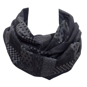 Könnte beinhalten: Ein dunkelgrauer Loop-Schal mit einem sich wiederholenden geometrischen Muster in Schwarz und Hellgrau. Der Schal besteht aus einem weichen Stoff und ist für das Tragen um den Hals konzipiert. Das Muster umfasst verschiedene Formen und Designs.