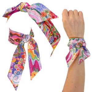 Può includere: Un foulard di seta colorato con un motivo floreale e astratto. Il foulard può essere indossato come una fascia per capelli o un braccialetto.