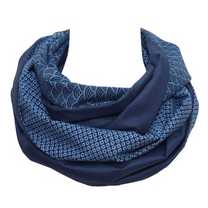 Könnte beinhalten: Ein marineblauer Loop-Schal mit einem geometrischen Muster in Blautönen. Der Schal hat ein sich wiederholendes Muster aus kleinen Quadraten und wellenartigen Designs. Der Schal ist aus weichem Stoff gefertigt und wird um den Hals getragen.