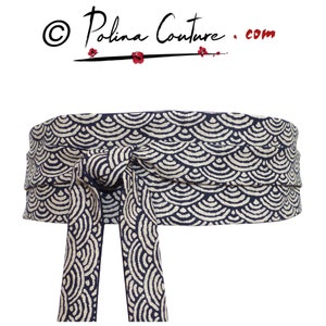 Può includere: Una cintura in tessuto blu navy e crema con un fiocco annodato. Il motivo è un disegno ripetitivo di linee curve che ricordano le onde.