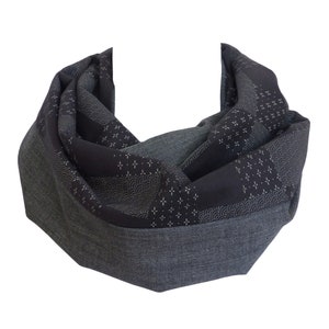 Peut inclure: Une écharpe infinie gris foncé avec un motif géométrique. L'écharpe présente un mélange de textures et de motifs, notamment de petits motifs floraux blancs et en forme de vagues. L'écharpe est faite d'un tissu doux et est conçue pour être portée autour du cou.