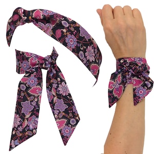 May include: A floral patterned headband, wrist wrap, and bow tie. The fabric features a dark background with pink, purple, and blue flowers. The wrist wrap is tied around a wrist.