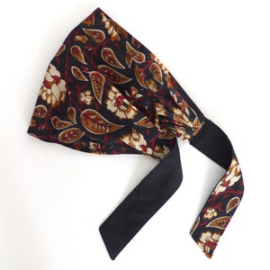 May include: A black headband with a floral print in shades of red, brown, and cream. The headband has a black fabric tie.