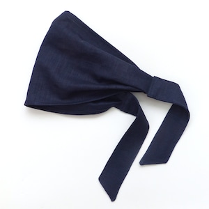 May include: A dark blue fabric headband with long ties. The headband is folded and tied in a knot at the back.
