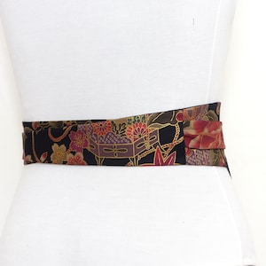 May include: A black fabric belt with a colorful floral and geometric pattern. The belt is tied in a bow at the front.