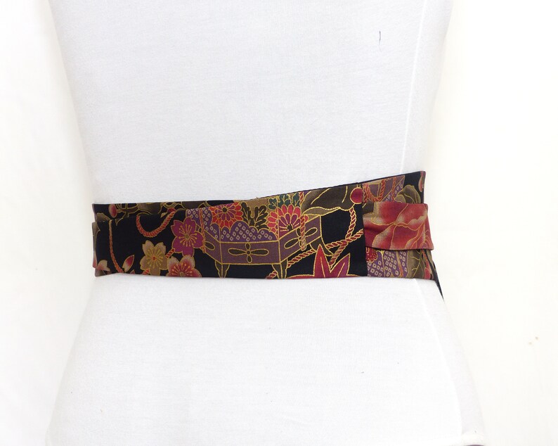 May include: A black fabric belt with a colorful floral and geometric pattern. The belt is tied in a bow at the front.