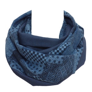 Könnte beinhalten: Ein blauer, gemusterter Infinity-Schal mit verschiedenen geometrischen und floralen Mustern.