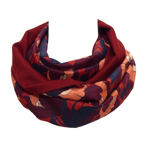 May include: A burgundy infinity scarf with a floral pattern in shades of orange, navy, and burgundy. The scarf is made of a soft material and is designed to be worn around the neck.
