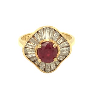 Puede incluir: Un anillo de oro con una piedra preciosa de rubí rojo rodeada por un halo de diamantes más pequeños.