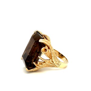 May include: A gold ring with a large, rectangular, dark brown gemstone set in a gold, leaf-like design.
