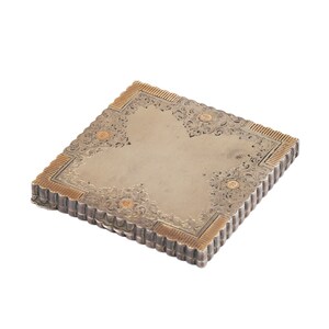 Puede incluir: Un estuche compacto de plata y oro con un dise&ntilde;o grabado ornamentado. El estuche tiene un borde festoneado y una tapa con bisagras.