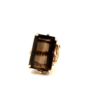 May include: A gold ring with a large, rectangular, smoky quartz gemstone. The ring has a delicate, ornate design.