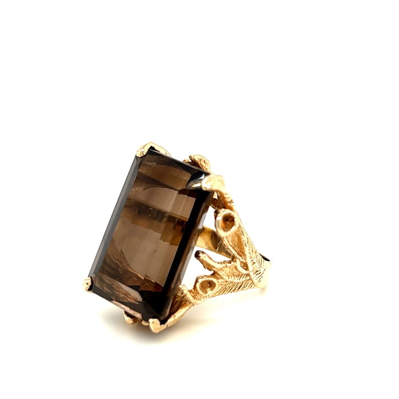 May include: A gold ring with a large, rectangular, smoky quartz gemstone. The ring has a delicate, leafy design.