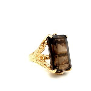 May include: A gold ring with a large, rectangular, smoky quartz gemstone. The ring has a detailed, ornate design.
