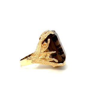 May include: A gold ring with a large, dark brown, faceted gemstone set in a stylized, leaf-like design.
