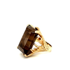 May include: A gold ring with a large, rectangular, smoky quartz gemstone. The ring band is designed with a stylized branch motif.