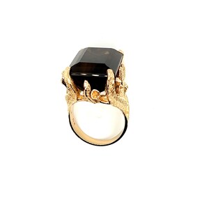 May include: A gold ring with a large, dark brown, emerald-cut gemstone. The ring band is intricately designed with a floral motif.