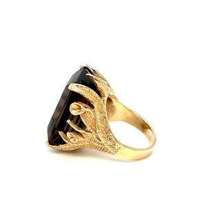 May include: A gold ring with a large, dark brown, rectangular gemstone set in a detailed, ornate, gold setting.