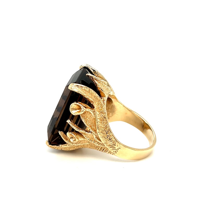 May include: A gold ring with a large, dark brown, rectangular gemstone set in a detailed, ornate, gold setting.