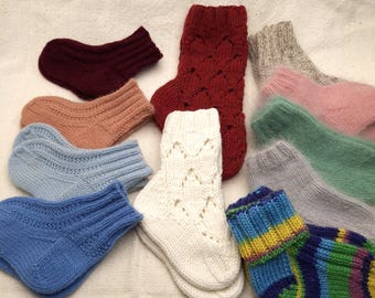 May include: A selection of hand-knitted socks in diverse colours, such as red, blue, pink, and white. The socks display various patterns and textures, highlighting the craftsmanship. The socks are arranged on a neutral-coloured surface.