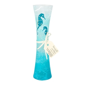May include: A blue glass vase with a white and blue ombre effect. The vase is decorated with two hand-painted seahorses. The vase is tied with a white ribbon and a tag that reads "Strawsilk on Glass by Karen Rose". Do not immerse or soak, use a lightly moistened cloth to clean.