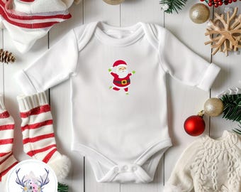 May include: A white long-sleeve baby bodysuit featuring a centered graphic of a smiling Santa Claus wearing a red suit with a black belt and green mittens. The garment has a round neckline and snap closures at the bottom for easy access.