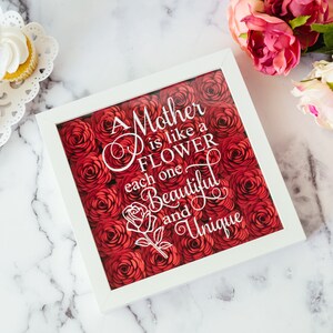 May include: A white framed artwork featuring the text "A Mother is like a Flower, each one Beautiful and Unique" set against a backdrop of red paper roses. Cupcakes and flowers are also in the image.
