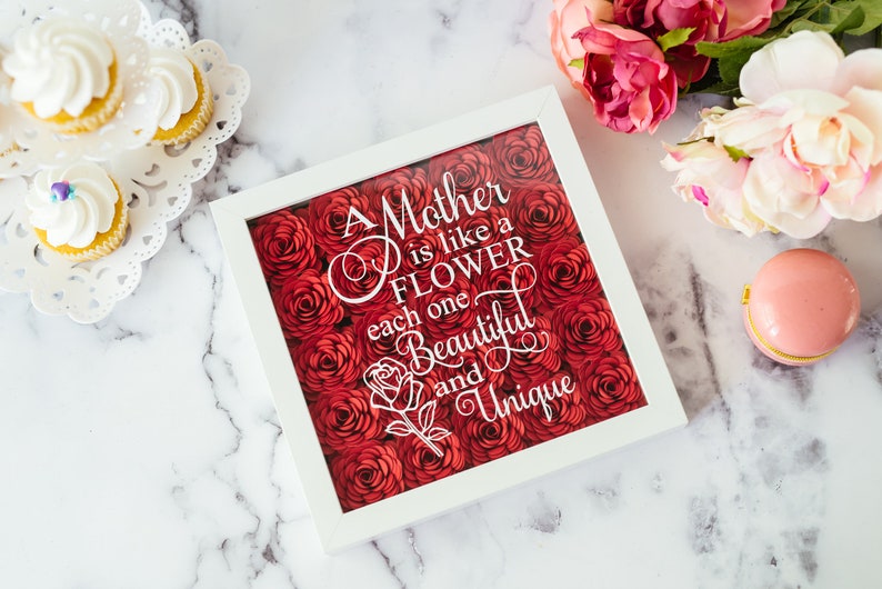 May include: A white framed artwork featuring the text "A Mother is like a Flower, each one Beautiful and Unique" set against a backdrop of red paper roses. Cupcakes and flowers are also in the image.