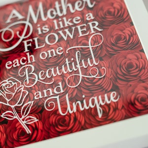 May include: A framed artwork with a background of red paper roses. White script reads, "A Mother is like a FLOWER, each one BEAUTIFUL and UNIQUE." A white rose outline is also present.