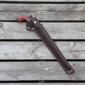 May include: A brown leather holster with a matching revolver. The holster is designed to hold a long-barreled firearm. The revolver has a wooden grip. The holster is stitched with white thread and has silver rivets.