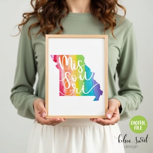 Può includere: Stampa incorniciata con il contorno dello stato del Missouri, riempita con un design ad acquerello arcobaleno. La parola "Missouri" è scritta in corsivo bianco. La cornice è di colore legno chiaro.