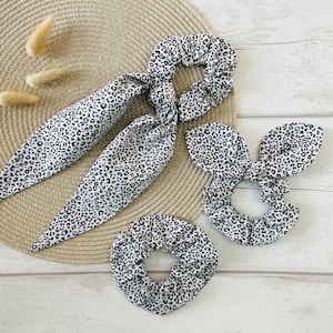 May include: Three black and white leopard print scrunchies. One is a long, tied scrunchie, and the other two are smaller, round scrunchies.