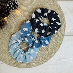May include: Three fabric hair scrunchies with a polar bear print. One scrunchie is black with white polar bears, one is blue with white polar bears, and one is light blue with white polar bears.