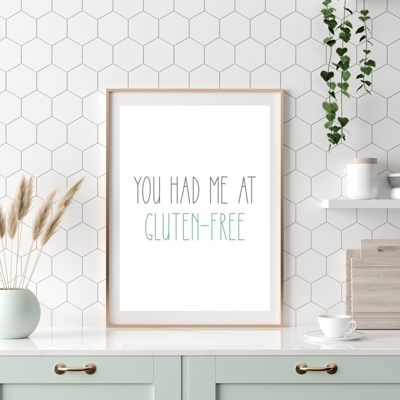 Pu&ograve; includere: Una stampa incorniciata con il testo "You had me at gluten-free" in un ambiente da cucina. La stampa &egrave; su sfondo bianco con testo nero. La cornice &egrave; in legno chiaro. La stampa &egrave; appoggiata su un piano di lavoro bianco davanti a uno schienale in piastrelle bianche.
