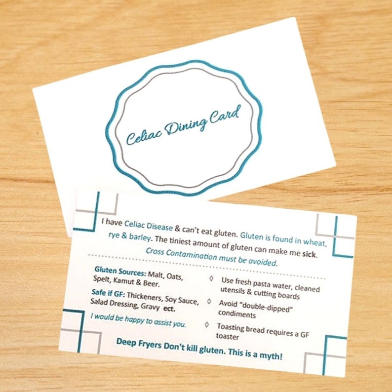 May include: A white Celiac Dining Card with blue text and a scalloped border. The card explains gluten-free requirements, listing sources like wheat, rye, and barley, and provides instructions for safe food preparation to avoid cross-contamination.