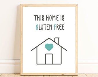 Può includere: Una stampa incorniciata bianca con il testo "This home is gluten free" in nero. Sotto il testo c'è un disegno a linea nera di una casa con un cuore turchese alla finestra.