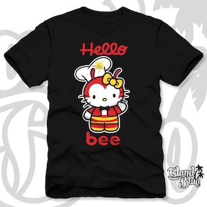 May include: Black t-shirt featuring a cartoon character with a red and yellow bee design. The text "Hello bee" is printed in red. The character wears a chef's hat and a yellow bow.