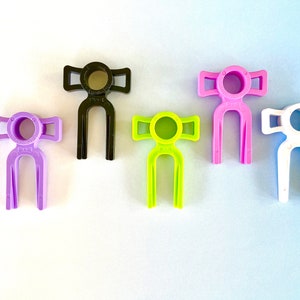 May include: Five plastic figures with a bow tie design. The figures are in different colours: purple, black, green, pink, and white.