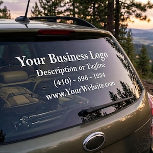 May include: The rear window of a car features a white decal with the text "Your Business Logo," a tagline, phone number, and website address. The car is olive green, parked outdoors with a forest and sunset in the background.