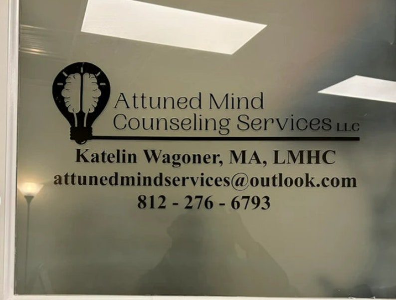 May include: A black and white image of a lightbulb with a brain inside. The text "Attuned Mind Counselling Services LLC" is below the image. The text "Katelin Wagoner, MA, LMHC" is below the text. The text "attunedmindservices@outlook.com" is below the text. The text "812-276-6793" is below the text.