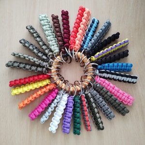 May include: A collection of colourful paracord keychains with a variety of patterns and designs. The keychains are attached to a metal ring.