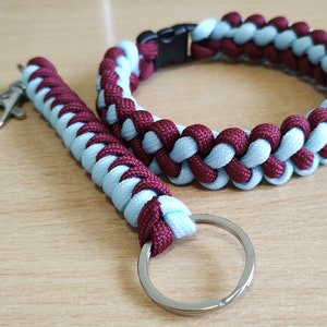 May include: A blue and burgundy paracord keychain with a silver key ring. The keychain is made of two strands of paracord that are woven together.