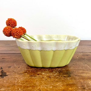 May include: A yellow and white ceramic bowl with a scalloped rim. The bowl is sitting on a wooden surface.
