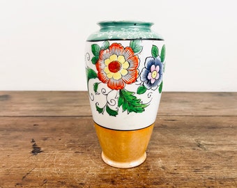 May include: A small, white ceramic vase with a green rim and floral design. The vase features a yellow, orange, and red flower with green leaves and a blue and pink flower with a yellow center.