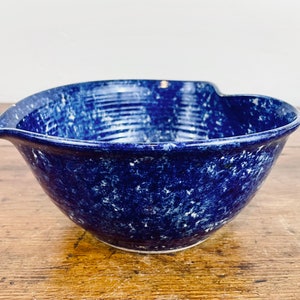 May include: A blue and white ceramic mixing bowl with a speckled glaze. The bowl has a unique shape with a pour spout on one side.
