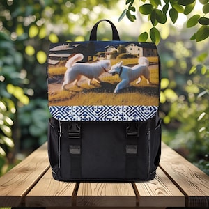 May include: Black backpack with a flap featuring a print of two white dogs playing in a field. The flap has a blue and white geometric pattern. The backpack has adjustable straps and side pockets.