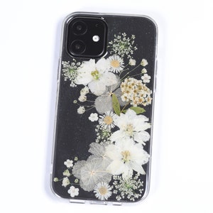 Clear phone case with a touch of glitter, adorned with an arrangement of natural pressed flowers in white and soft beige, accented with green leaves, offering a sparkling and delicate floral design, available from SunnyPigStudio.